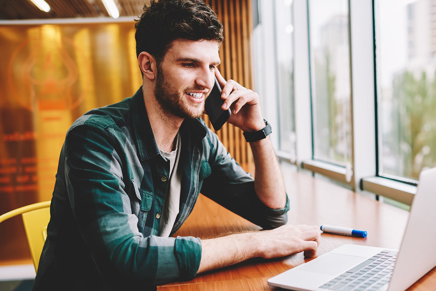 man talks on cell phone in front of laptop